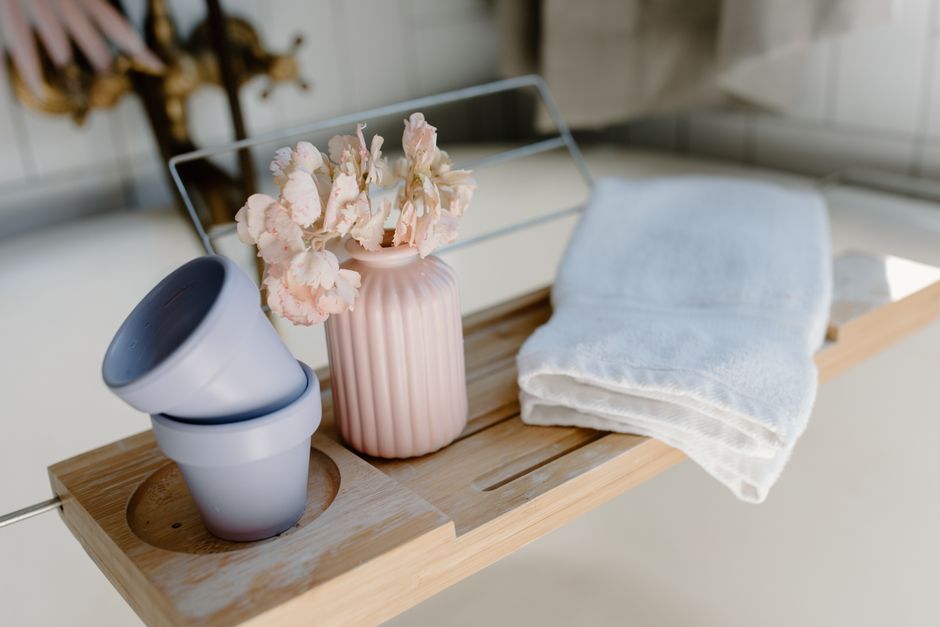 Aesthetic bathroom setup featuring a pink ceramic vase with flowers on a wooden tray, offering a touch of elegance.