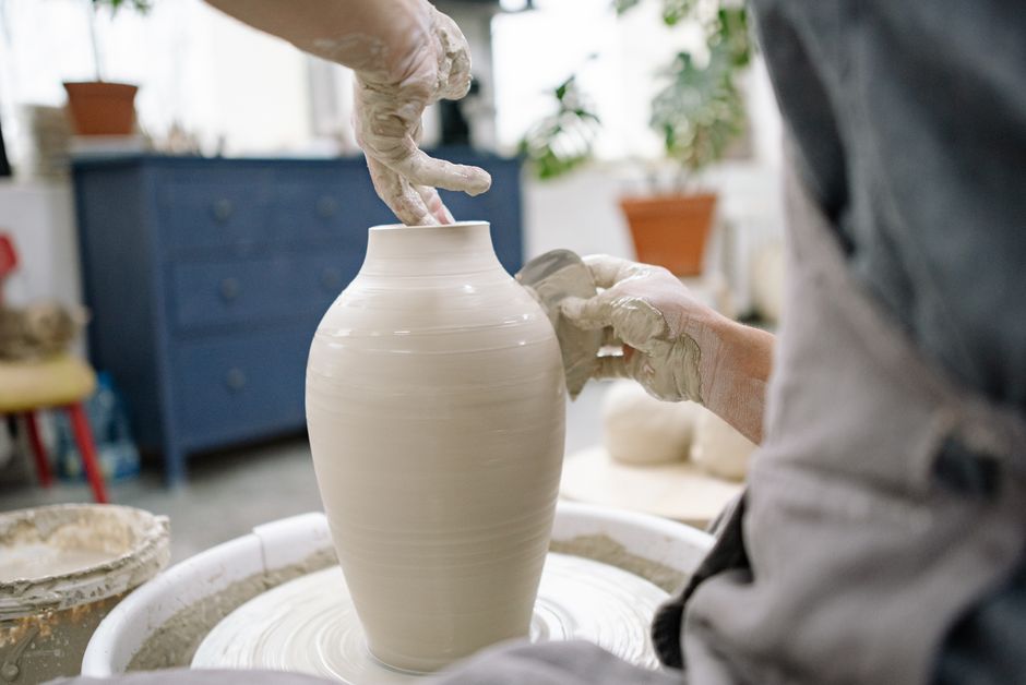 Craftsman skillfully shapes pottery vase on wheel in a bright workshop setting.