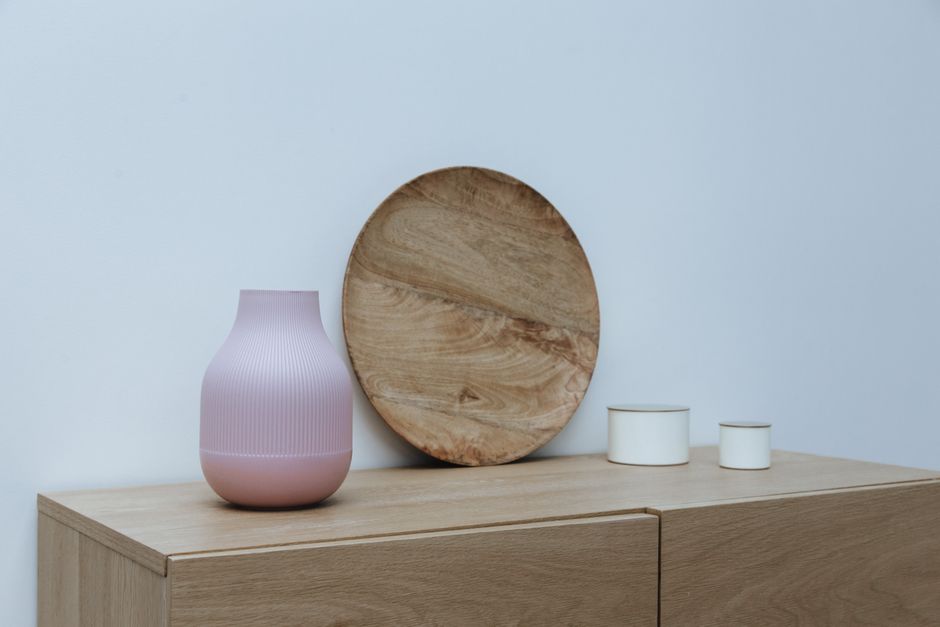 Stylish minimalist interior setup featuring wooden decor and a pink vase on light wooden furniture.